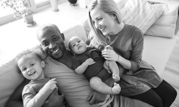 Ein Mann und eine Frau sitzen mit ihren beiden Kindern auf einer weißen Couch. Alle lachen. Im Hintergrund ist ein Fenster erkennbar.
