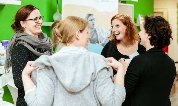 Das Bild zeigt vier Frauen, die sich unterhalten vor einer grünen Wand und hellen Leinwand.
