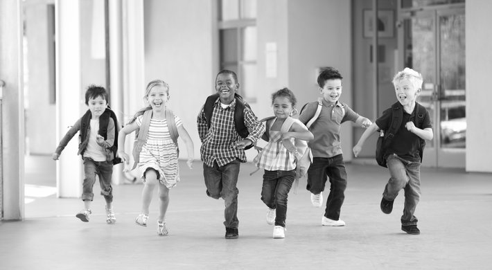 Eine Gruppe von Kindern, die Rucksäcke tragen, kommen freudig angerannt. 