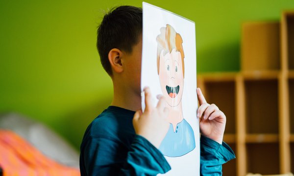 Das Bild zeigt einen Jungen hinter einem Papier mit einem Gesicht darauf